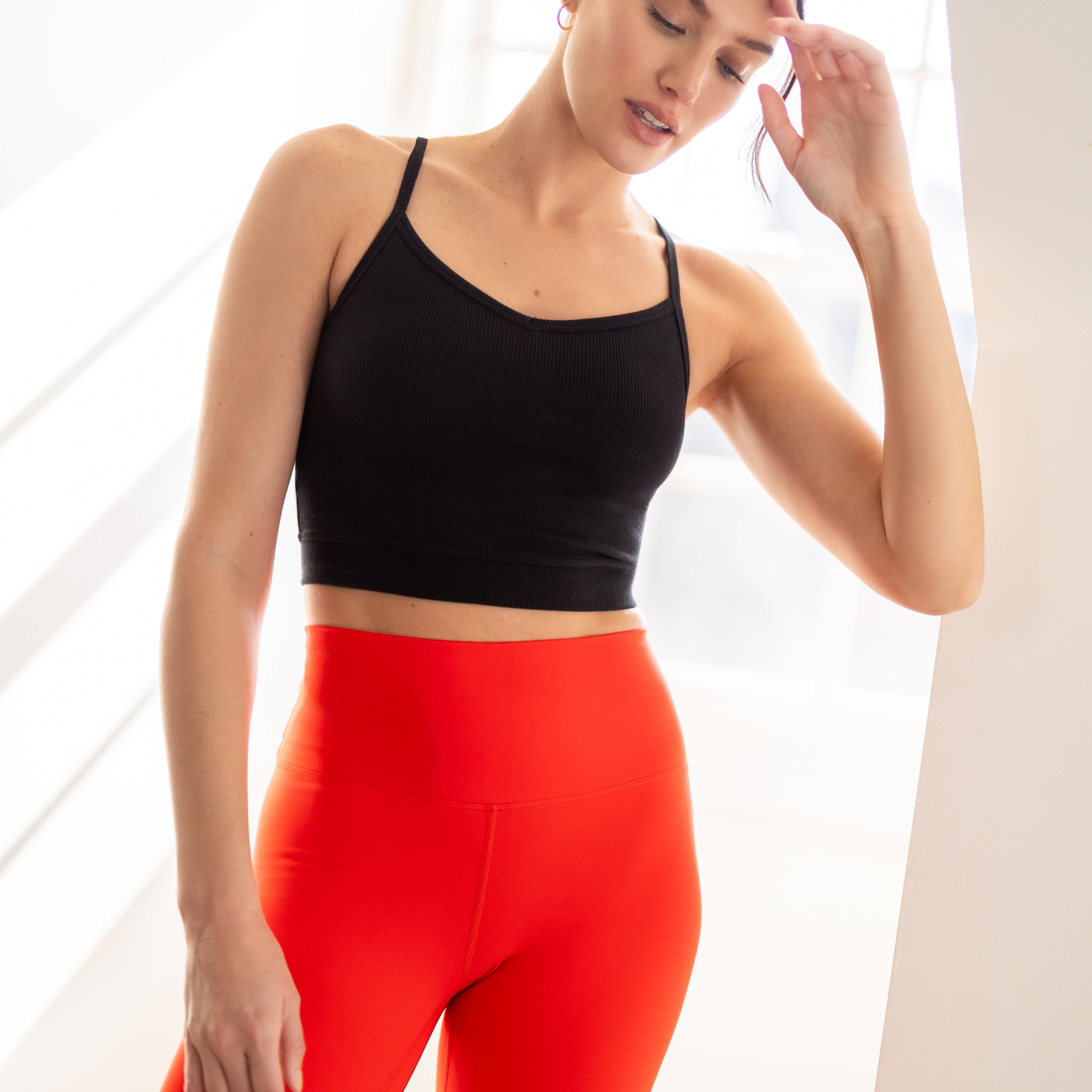 A woman wearing Tap Shoe Black bralette with thin straps and a ribbed texture with red leggings on white background.