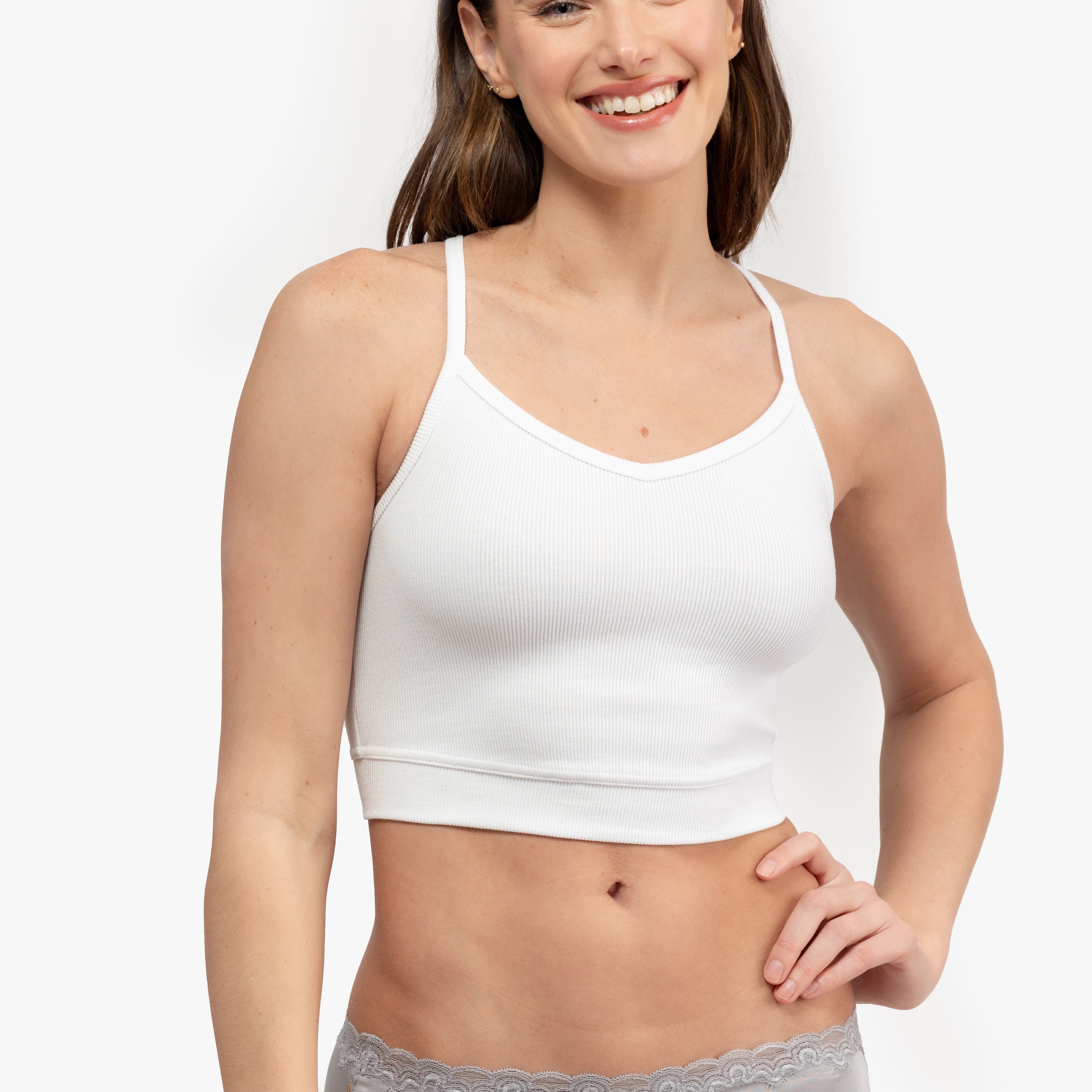 A woman wearing a white bralette with thin straps and a ribbed texture on white background.