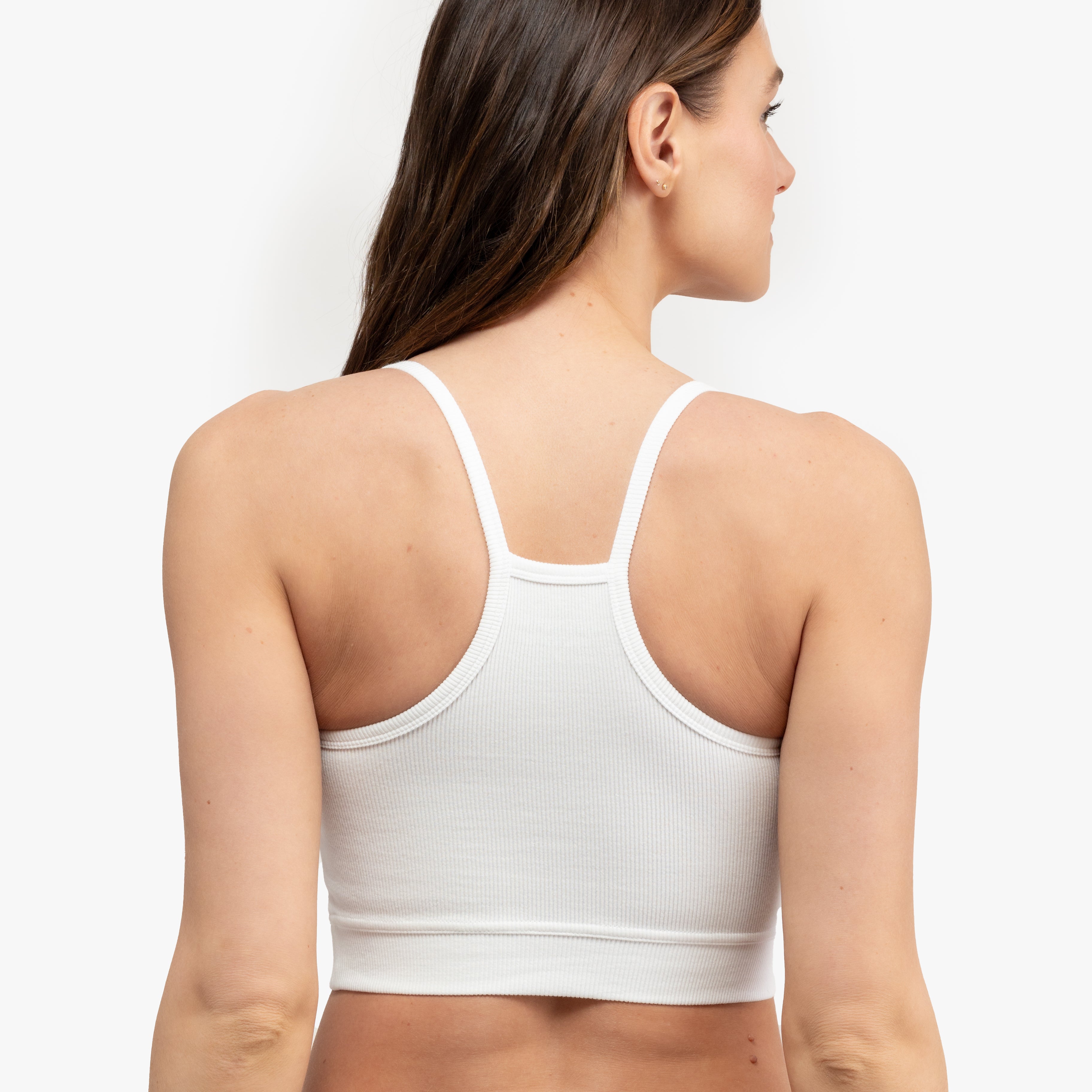 A woman wearing a white bralette with thin straps and a ribbed texture on white background.