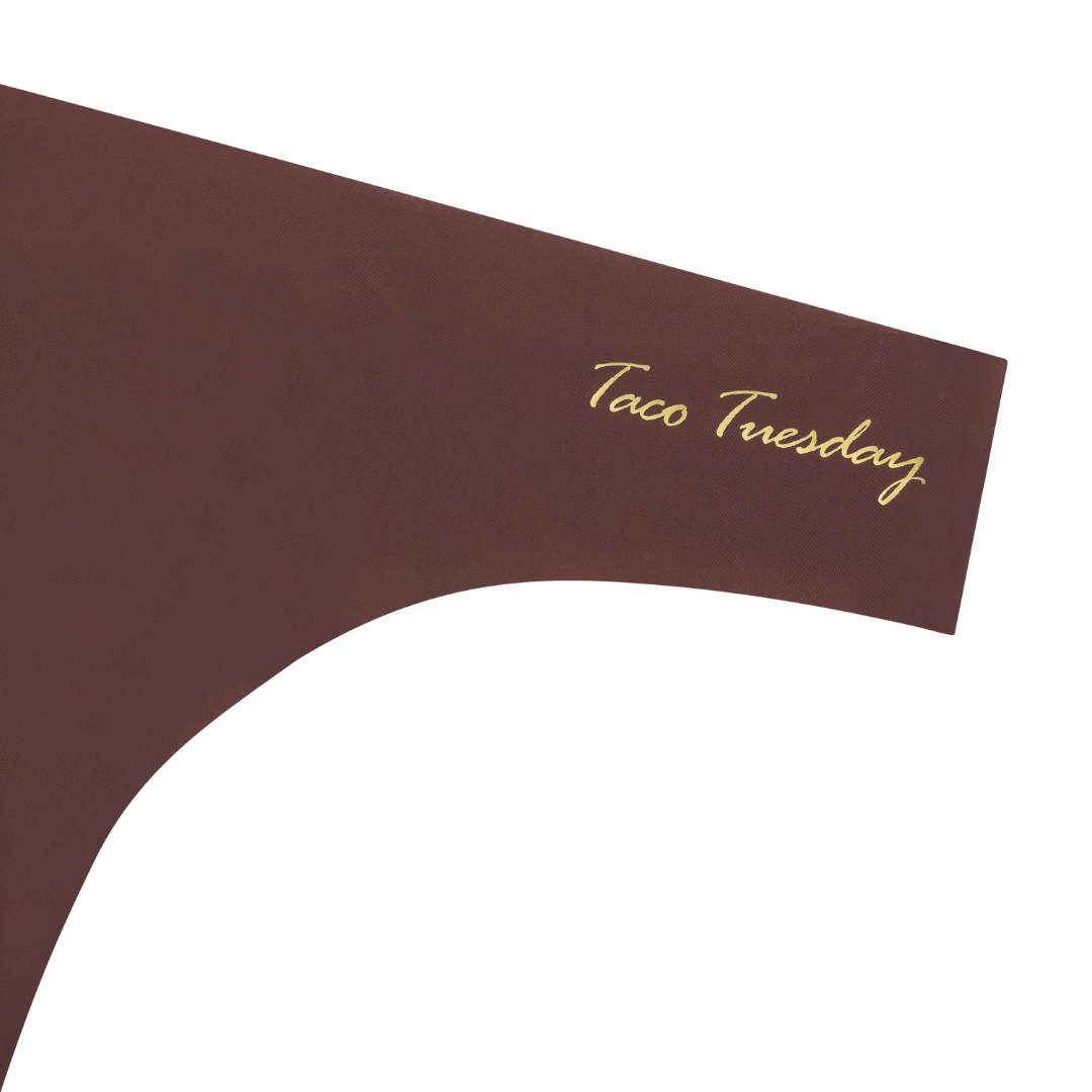 A chocolate soft seamless thong with 'Taco Tuesday' written in gold on the front.