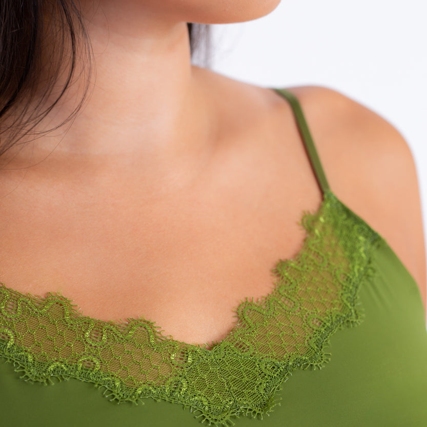 A woman wearing a green soft seamless camisole with delicate lace detail at the neckline, with adjustable straps.