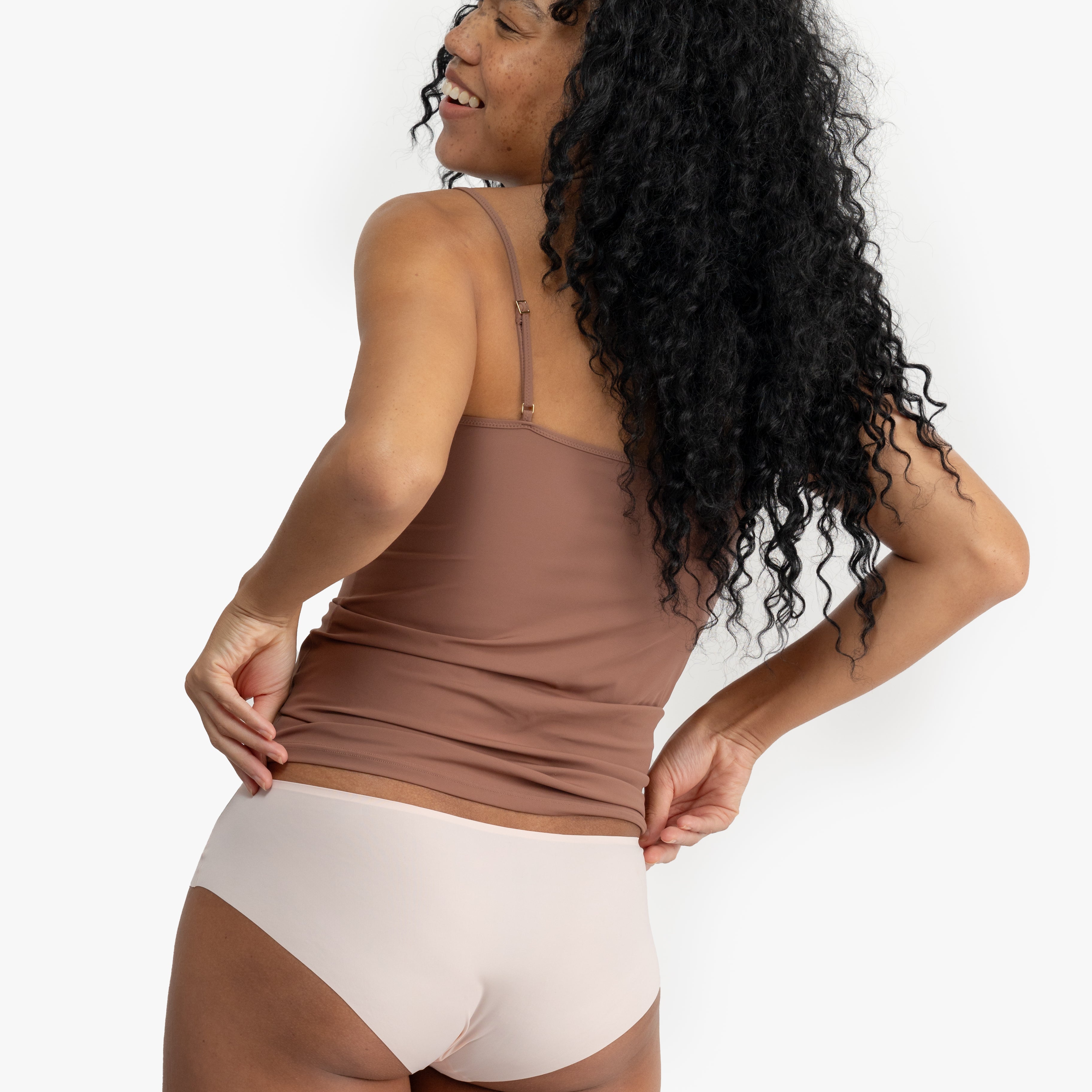 Woman wearing a soft seamless camisole with adjustable spaghetti straps and a V-neckline on white background.