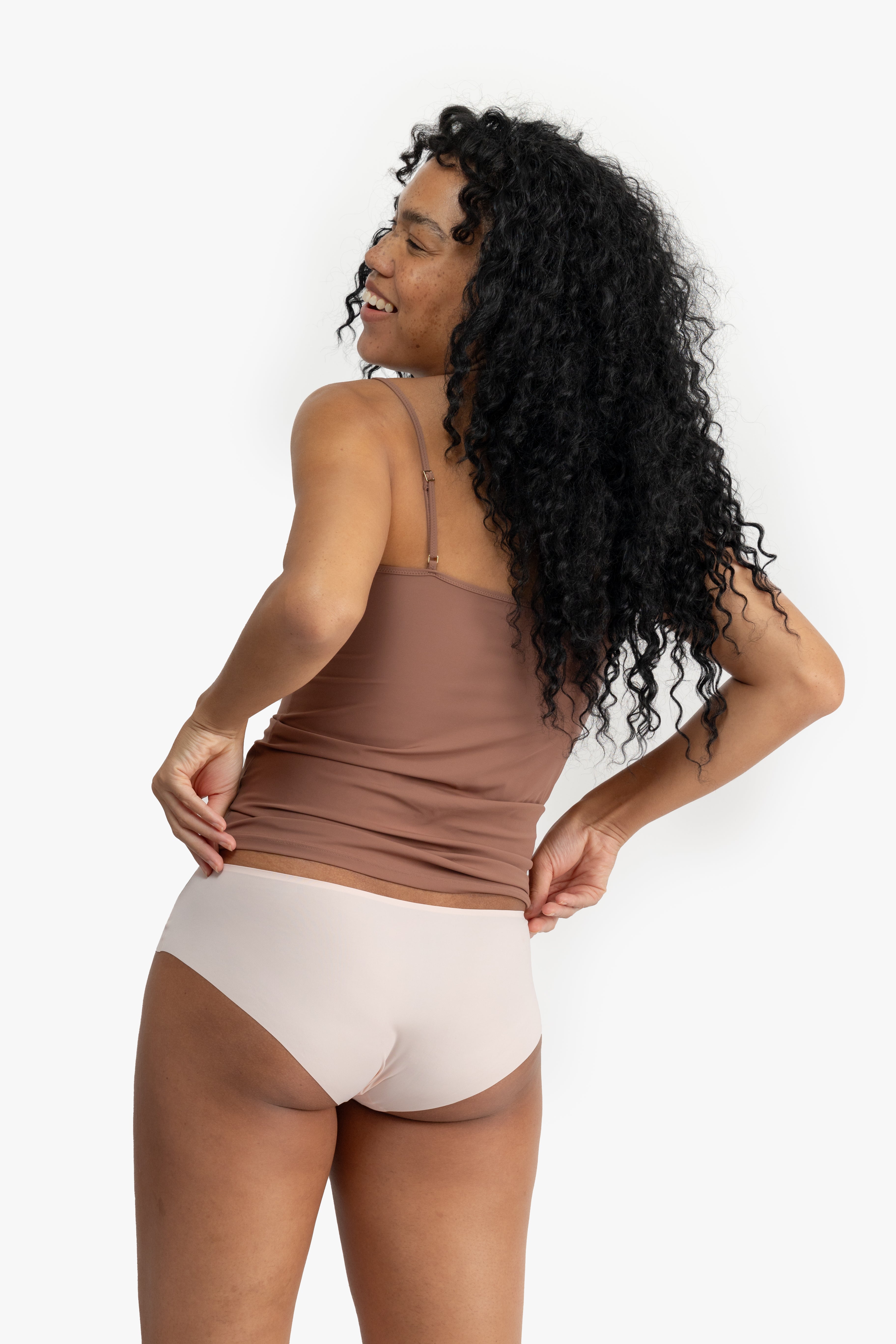 Woman wearing a soft seamless camisole with adjustable spaghetti straps and a V-neckline on white background.