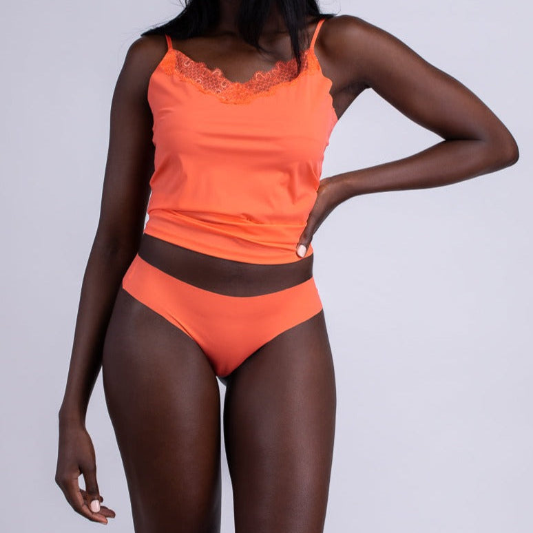 A woman wearing an orange soft seamless thong underwear and camisole on white background.