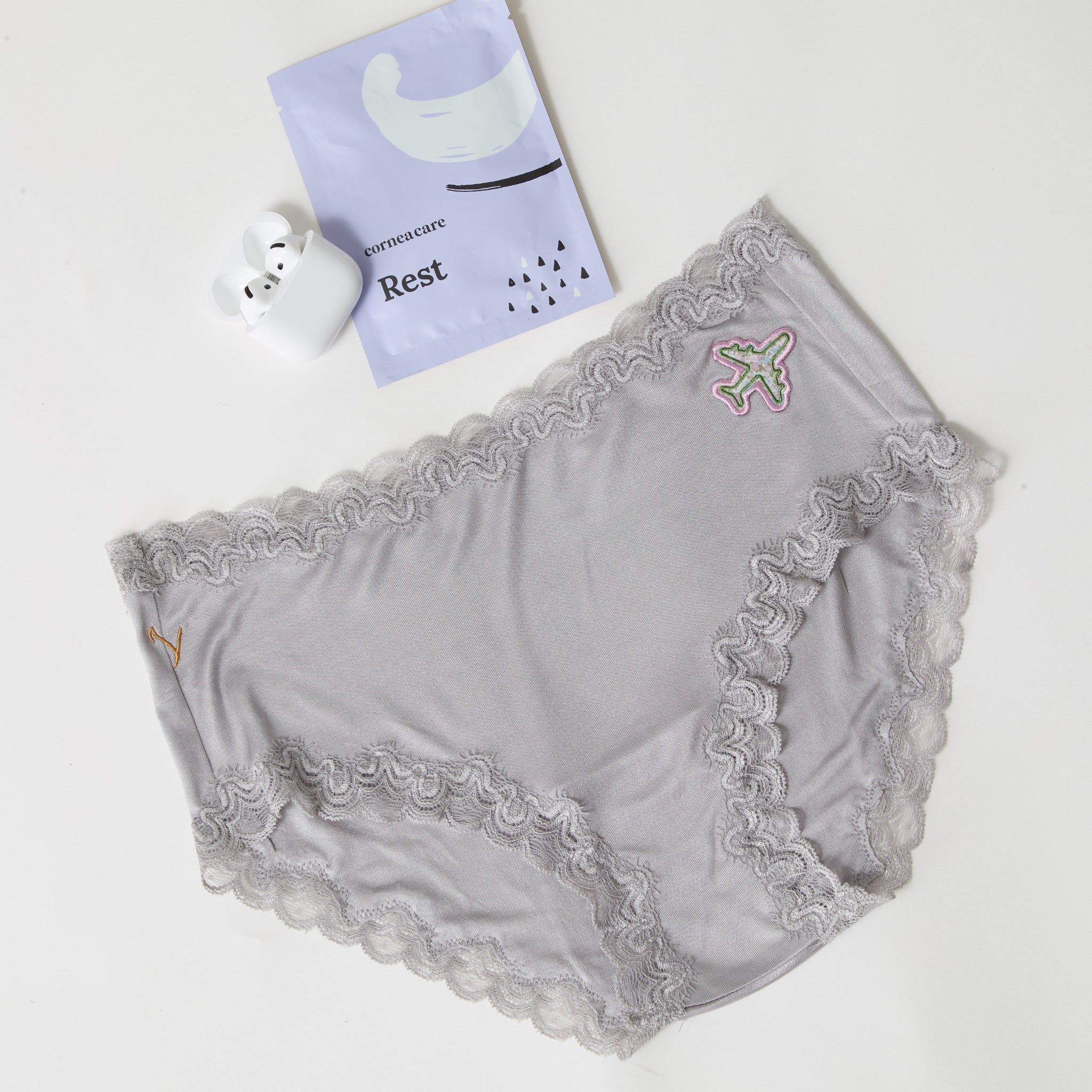 Soft Silk Brief with airplane patch flay lay with airpods and eye patches on a white background.
