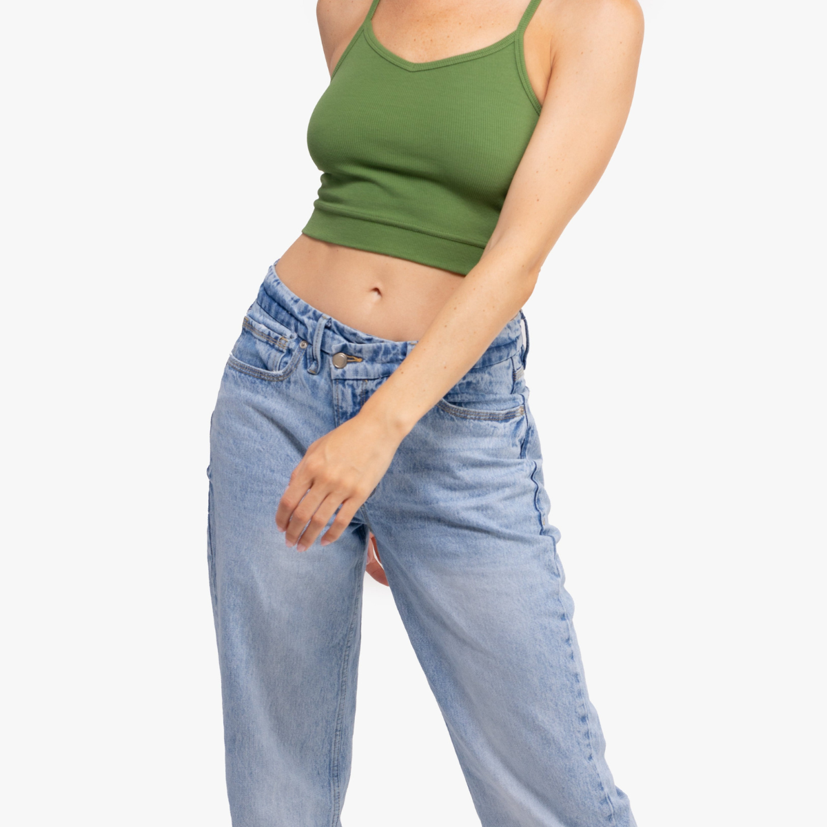 A woman waring a Kale bralette with thin straps and a ribbed texture and jeans on white background.