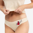 A woman wearing a soft seamless smoke grey thong underwear with an embroidered floral pattern in contrasting colors against white background.
