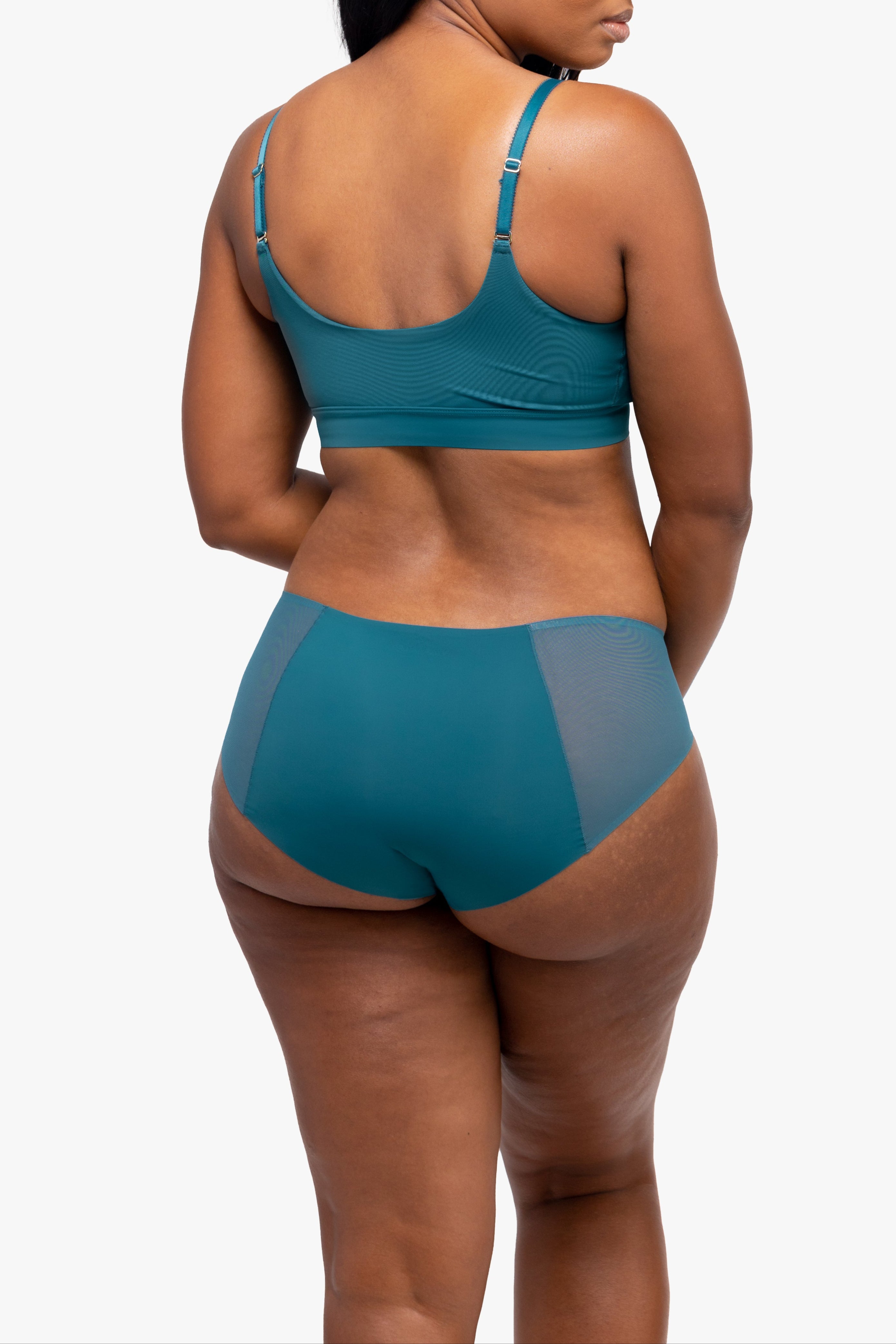 Woman wearing a teal sports bra and high-waisted underwear set on a white background