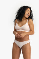 Woman wearing a rose quartz soft seamless thong underwear on white background.