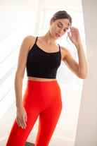 A woman wearing Tap Shoe Black bralette with thin straps and a ribbed texture with red leggings on white background.