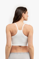 A woman wearing a white bralette with thin straps and a ribbed texture on white background. 