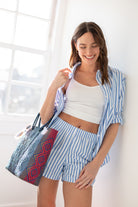 A woman wearing a white bralette with thin straps and a ribbed texture with striped shorts and shirt on white background.