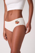Model wearing Uwila Warrior Soft Seamless Winter White Brief with Orange Blossom Embroidery on White Background.