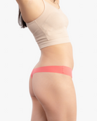 A woman wearing a calypso coral soft seamless thong underwear on white background.