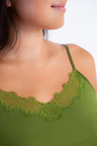 A woman wearing a green soft seamless camisole with delicate lace detail at the neckline, with adjustable straps.