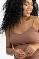 Woman wearing a toffee soft seamless camisole with adjustable spaghetti straps and a V-neckline on white background.