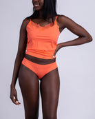 A woman wearing an orange soft seamless thong underwear and camisole on white background.