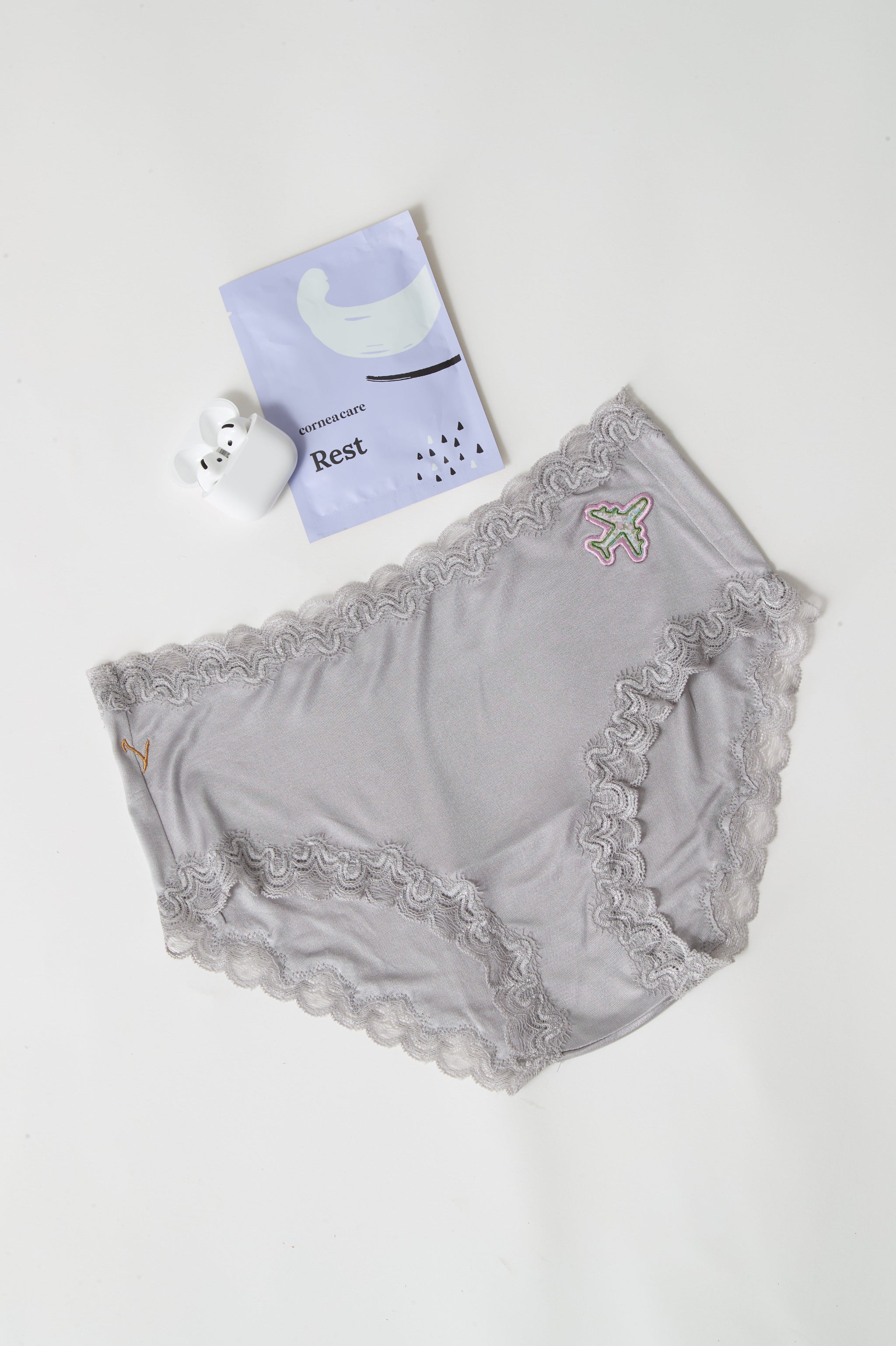 Soft Silk Brief with airplane patch flay lay with airpods and eye patches on a white background. 