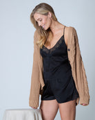 Woman wearing a black lace camisole and short set with a beige cardigan on a light gray background