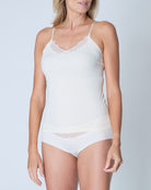 Woman wearing a winter white soft seamless lace-trimmed camisole against light gray background.