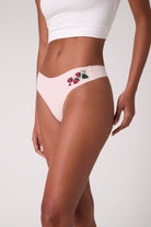 Model wearing Uwila Warrior Soft Seamless Thong with Wild Strawberry embroidery on white background. 