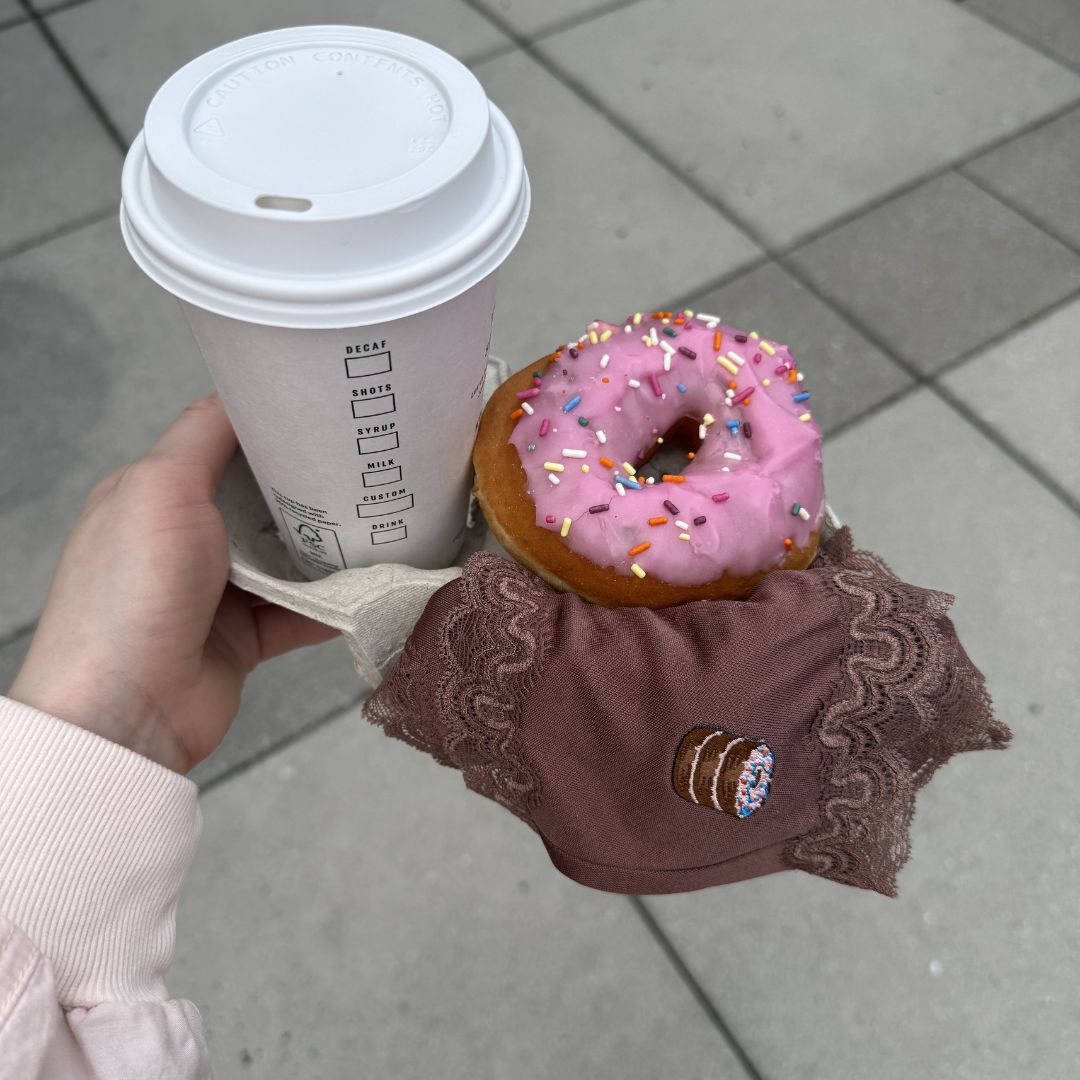 Hand holding a coffee cup with a pink donut with Uwila Warrior Toffee Soft Silk Brief hanging off the tray.