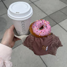Hand holding a coffee cup with a pink donut with Uwila Warrior Toffee Soft Silk Brief hanging off the tray.