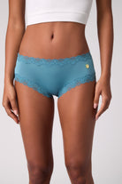 Model wearing Uwila Warrior Storm Blue Soft Silk Briefs with Lime embroidered patch on white background.