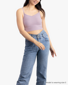A woman wearing a nirvana bralette with thin straps and a ribbed texture  and jeans on white background.