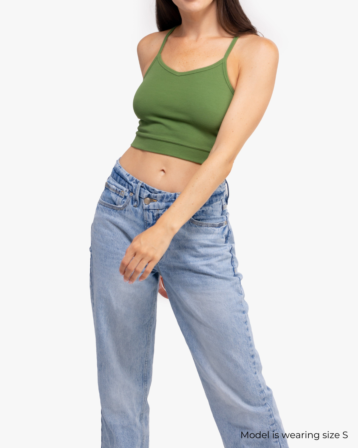 A woman waring a Kale bralette with thin straps and a ribbed texture and jeans on white background.